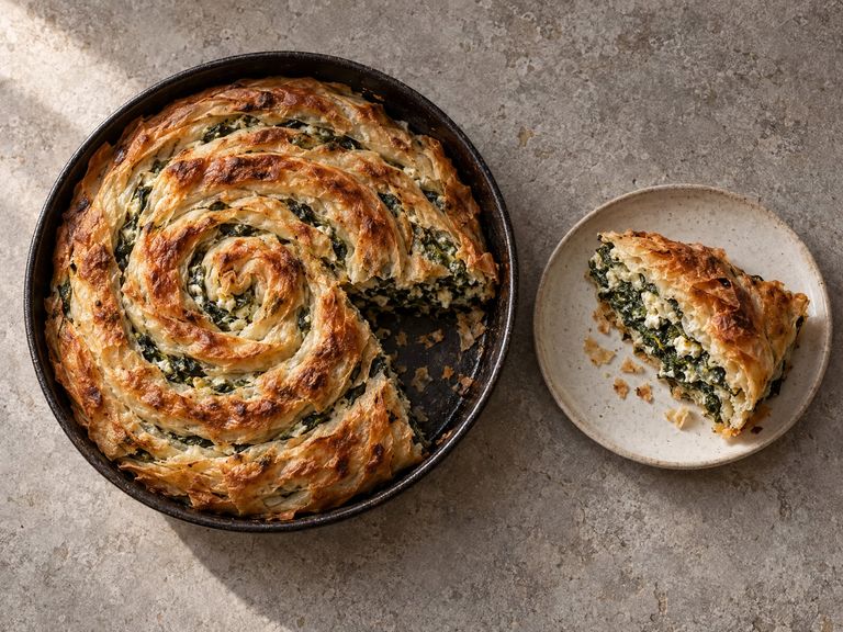 Spinach and cheese pita in a round pan, with a slice cut and served on a plate