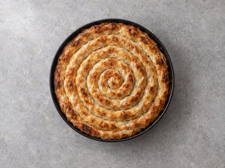 A whole spiral pita, golden and flaky, in a round pan